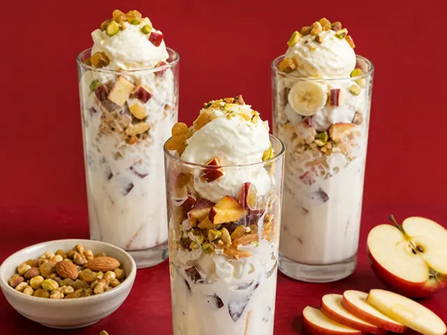 Three tall glasses of ice cream layered with apple, banana and nuts