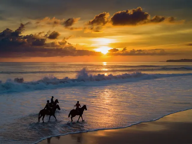 Riders on horseback at the edge of the surf, the sun going down into the sea behind them