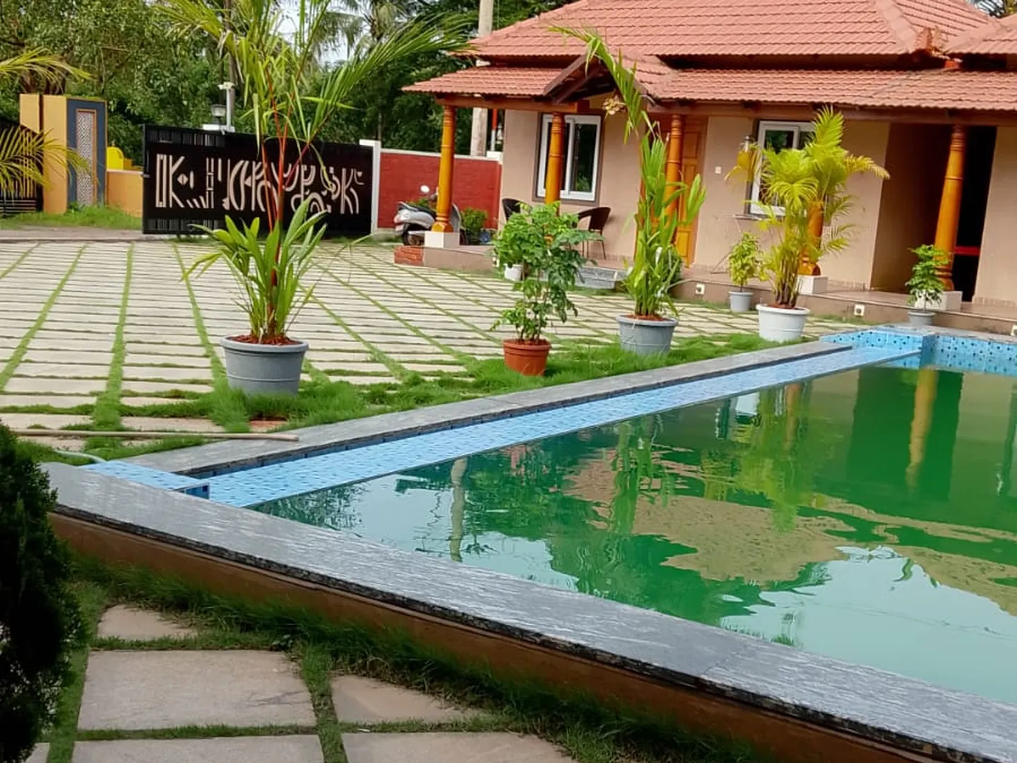 Paved poolside with plants and a tiled-roof cottage behind